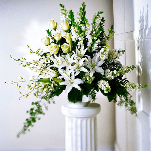 A Solemn Tribute is reflected in this arrangement of all White Roses, Snapdragons, Stargazer Lilies, Stock and Dendrobium Orchids. Fragrant.  Approximate size: 32”H x 40”W  FTD19-3155