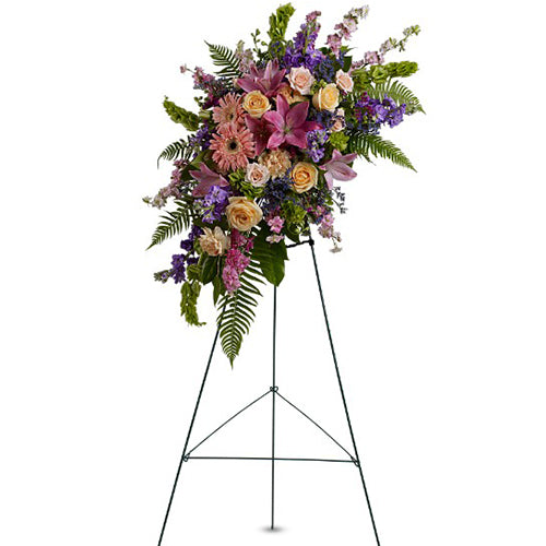 The beauty of a graceful spirit is reflected in this Tribute. Soft hued blooms in harmonious shades of peach, pink, purple and raspberry: Roses, stock larkspur, lilies, carnations and Bells of Ireland all grace this beautiful spray.  Arrangement size: 23”W x 29H. (Dimensions do not include easel.)  TFWEB531