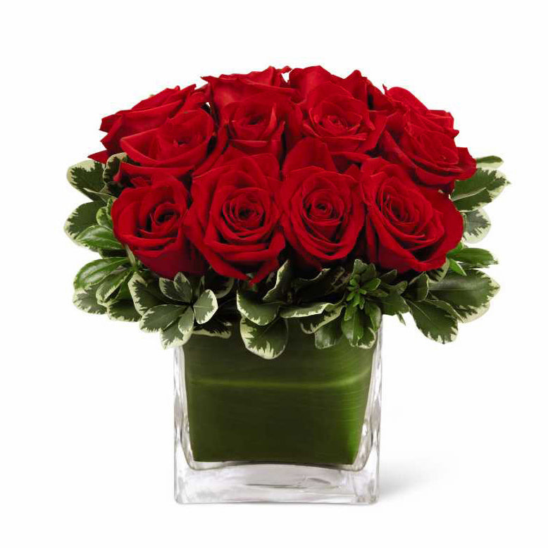 A Dozen Gorgeous Red Roses are Clustered Together and Surrounded By Variegated GreensA Dozen Gorgeous Red Roses are Clustered Together and Surrounded By VariegatedGreens for Maximum Impact. A tropical Ti-leaf Leaf Lines the Contemporary Square Vase for a finishing detail.   Approximate size: 8”H x 7”W 5 “ square vase.