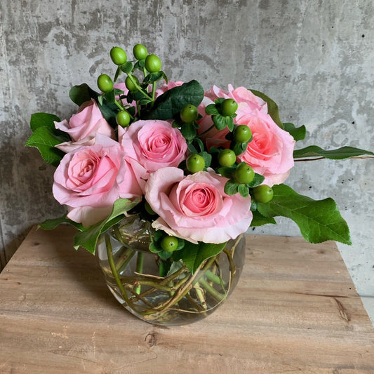 A romantic arrangement of nine (9) roses with greenery in a low clear glass vase Available in a variety of colors. $80 and $100 size.
